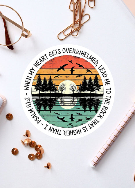 a circular sticker with a sunset and birds design, surrounded by various office supplies such as pens, a notebook, and a pair of glasses.