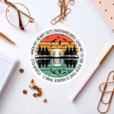 a circular sticker with a sunset and birds design, surrounded by various office supplies such as pens, a notebook, and a pair of glasses.