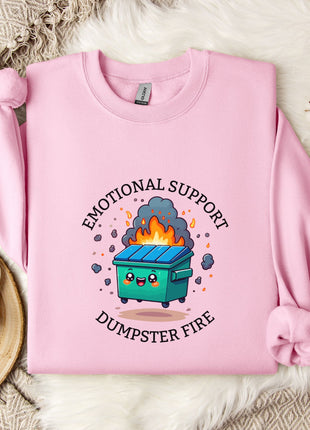 A pink sweatshirt with a graphic design depicting a fire inside a dumpster, accompanied by the text "Emotional Support Dumpster Fire".