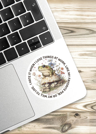 a sticker with a frog on a mushroom, placed on a laptop keyboard.
