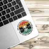A sticker with a sunset and forest design is placed on the edge of a laptop keyboard.
