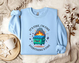 A light blue sweatshirt with a graphic design depicting a trash can on fire, accompanied by the text "It's fine, I'm fine Everything's fine".