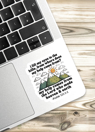 A sticker with a religious message is placed on a laptop keyboard, with a wooden surface in the background.