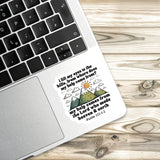 A sticker with a religious message is placed on a laptop keyboard, with a wooden surface in the background.