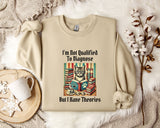 a beige sweatshirt with a printed design of a cat surrounded by books and a cup of coffee, along with the text "I'm Not Qualified To Diagnose But I Have Theories".