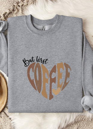 A gray sweatshirt with a heart-shaped design and the text "But first coffee" printed on it, along with a mug and some cotton balls.