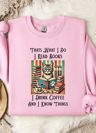 A pink sweatshirt with a cat illustration and text, along with a mug and a branch of cotton flowers, all placed on a white fur rug.