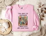 A pink sweatshirt with a cat illustration and text, along with a mug and a branch of cotton flowers, all placed on a white fur rug.