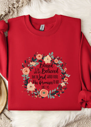 A red sweater with a floral design and text printed on it, along with a white mug and a branch of cotton flowers, all placed on a white fur rug.