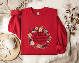 A red sweater with a floral design and text printed on it, along with a white mug and a branch of cotton flowers, all placed on a white fur rug.
