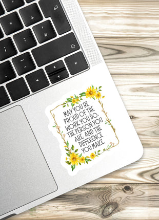 A sticker with a quote about pride and work is placed on the edge of a laptop keyboard.