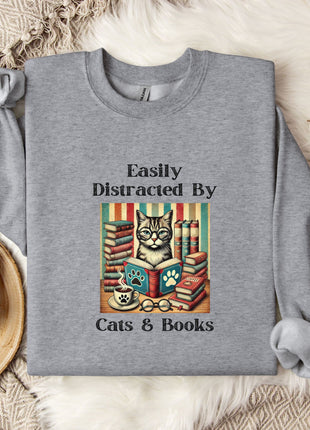a gray sweatshirt with a graphic design of a cat surrounded by books, along with the text "Easily Distracted By Cats & Books".