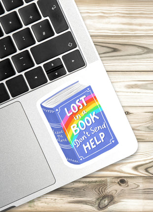 A sticker with the text "LOST IN A BOOK DON'T SEND HELP" is placed on the side of a laptop keyboard.