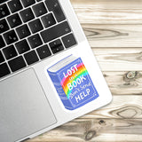 A sticker with the text "LOST IN A BOOK DON'T SEND HELP" is placed on the side of a laptop keyboard.