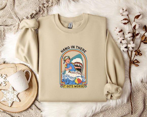 a beige sweatshirt with a graphic design depicting a person holding a shark and the text 