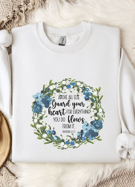 A white t-shirt with a floral design and text printed on it, placed on a bed with a white blanket and a white mug.
