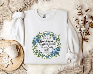 A white t-shirt with a floral design and text printed on it, placed on a bed with a white blanket and a white mug.