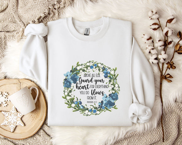 A white t-shirt with a floral design and text printed on it, placed on a bed with a white blanket and a white mug.