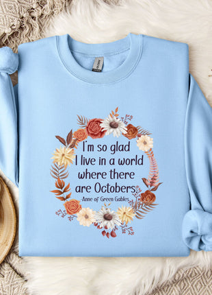 A light blue sweatshirt with a floral wreath design and a quote printed on it, placed on a bed with a white blanket and a white mug.