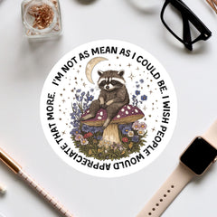 A sticker featuring a raccoon sitting on a mushroom surrounded by flowers and a crescent moon, with the text "I'm not as mean as I could be. I wish people would stop being mean."