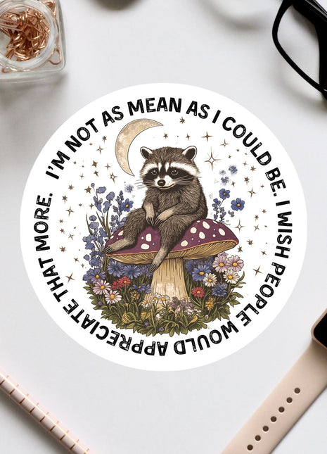 A sticker featuring a raccoon sitting on a mushroom surrounded by flowers and a crescent moon, with the text "I'm not as mean as I could be. I wish people would stop being mean."