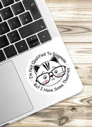 A sticker with a cat wearing glasses and the text "I'm Not Qualified To Diagnose, But I Have Some Theories" is placed on a laptop keyboard.