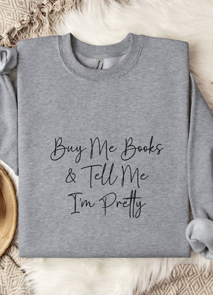 a gray sweatshirt with the text "Buy Me Books & Tell Me I'm Pretty" printed on it, along with a mug and some cotton balls.