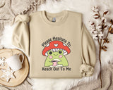 a beige sweater with a mushroom character and text, along with a mug, a plant, and some white flowers on a white fur rug.