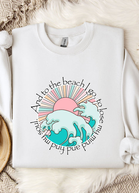 A white sweatshirt with a graphic design of a beach scene, including a sun, waves, and a palm tree, along with the text "And to the beach I go to lose my mind and push my limits".