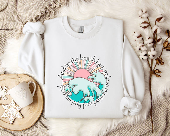 A white sweatshirt with a graphic design of a beach scene, including a sun, waves, and a palm tree, along with the text 