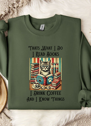 A green sweatshirt with a printed design of a cat surrounded by books and a cup of coffee, along with text that says "Thats what I do I read books I drink coffee and I know things".