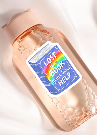 A pink bottle with a label that says "LOST IN A BOOK DON'T SEND HELP" and features a rainbow graphic.
