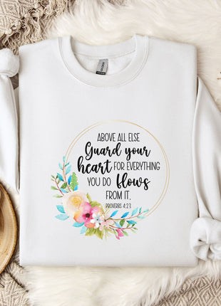 a white t-shirt with a floral design and text printed on it, placed on a bed with a white blanket and a white mug.