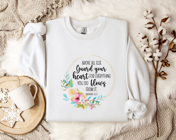 a white t-shirt with a floral design and text printed on it, placed on a bed with a white blanket and a white mug.