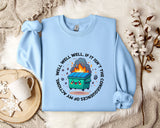 A light blue sweatshirt with a graphic design featuring a cartoon trash can with flames coming out of it, surrounded by a circular design with the text "WELL WELL, IF IT ISN'T THE CONSEQUENCES OF MY ACTION".