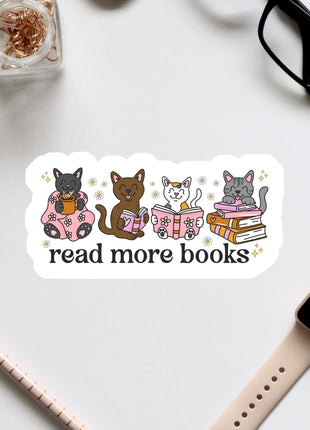 a sticker with a group of cats sitting on books, along with the text "read more books" written on it. The sticker is surrounded by various office supplies, such as a pair of glasses, a pen, and a notebook.