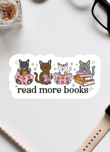 a sticker with a group of cats sitting on books, along with the text "read more books" written on it. The sticker is surrounded by various office supplies, such as a pair of glasses, a pen, and a notebook.