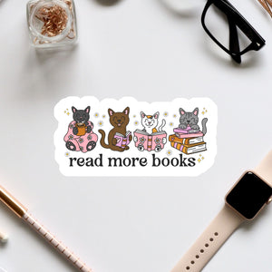 a sticker with a group of cats sitting on books, along with the text "read more books" written on it. The sticker is surrounded by various office supplies, such as a pair of glasses, a pen, and a notebook.