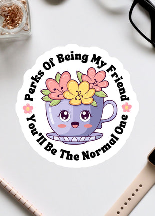 A sticker with a cartoon cup and flowers, surrounded by text that says "Perks Of Being My Friend You'll Be The Normal One".