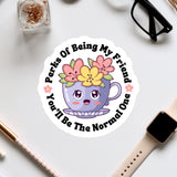 A sticker with a cartoon cup and flowers, surrounded by text that says "Perks Of Being My Friend You'll Be The Normal One".