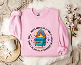 A pink sweatshirt with a graphic design featuring a cartoon dumpster with flames coming out of it, surrounded by text that reads "WELL WELL, IF IT ISN'T THE CONSEQUENCES".