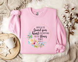 A pink sweatshirt with a floral design and text printed on it, placed on a white fur rug.