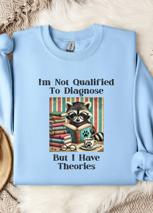 A light blue sweatshirt with a graphic design of a raccoon wearing glasses and surrounded by books, along with text that reads "I'm Not Qualified To Diagnose But I Have Theories".