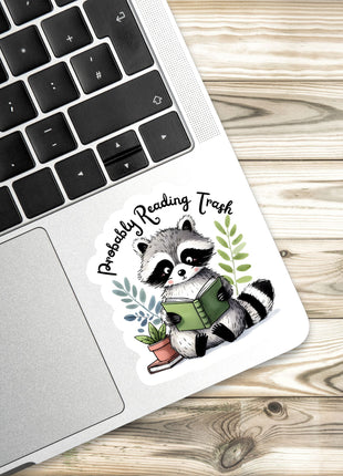 a sticker of a raccoon reading a book