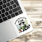 a sticker of a raccoon reading a book