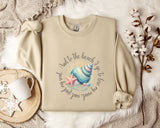 a beige sweatshirt with a graphic design of a seashell and starfish, along with the text "And to the beach go, to lose". The sweatshirt is laid out on a bed with a white blanket and a white mug. There are also some white flowers and a white snowflake in the scene.