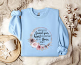 A light blue sweatshirt with a floral design and text printed on it, placed on a white fur rug.