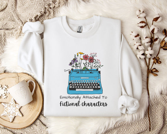 A white sweatshirt with a graphic design of a typewriter filled with colorful flowers, accompanied by the text 