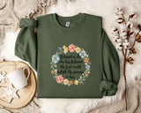 A green sweatshirt with a floral design and text printed on it, along with a mug and some white flowers on a white surface.