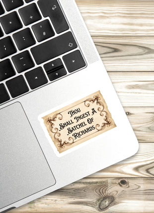 A sticker with a quote is placed on the edge of a laptop keyboard, resting on a wooden surface.